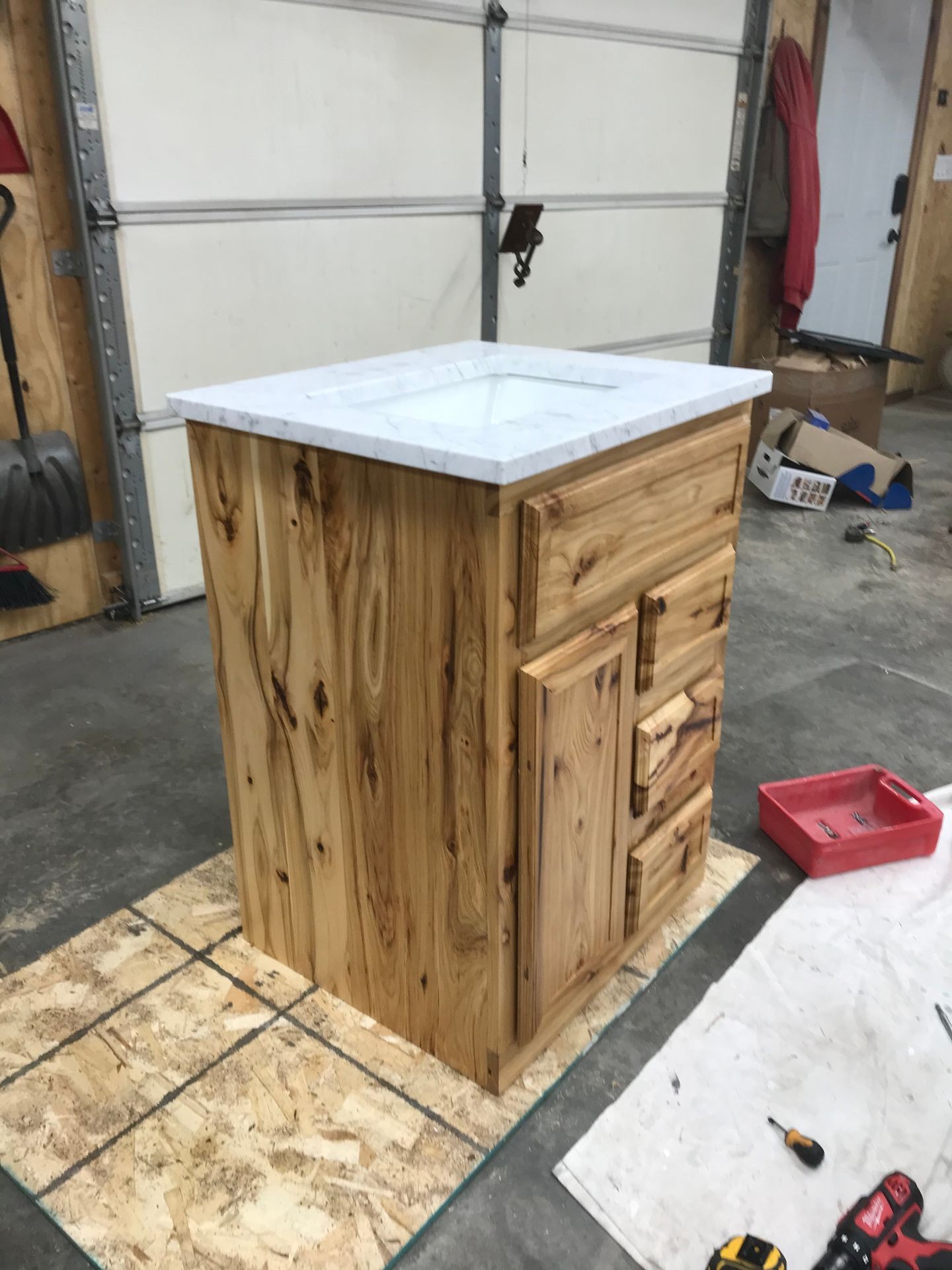 Wooden kitchen cabinet with marble countertop in a workshop, surrounded by tools and construction materials.