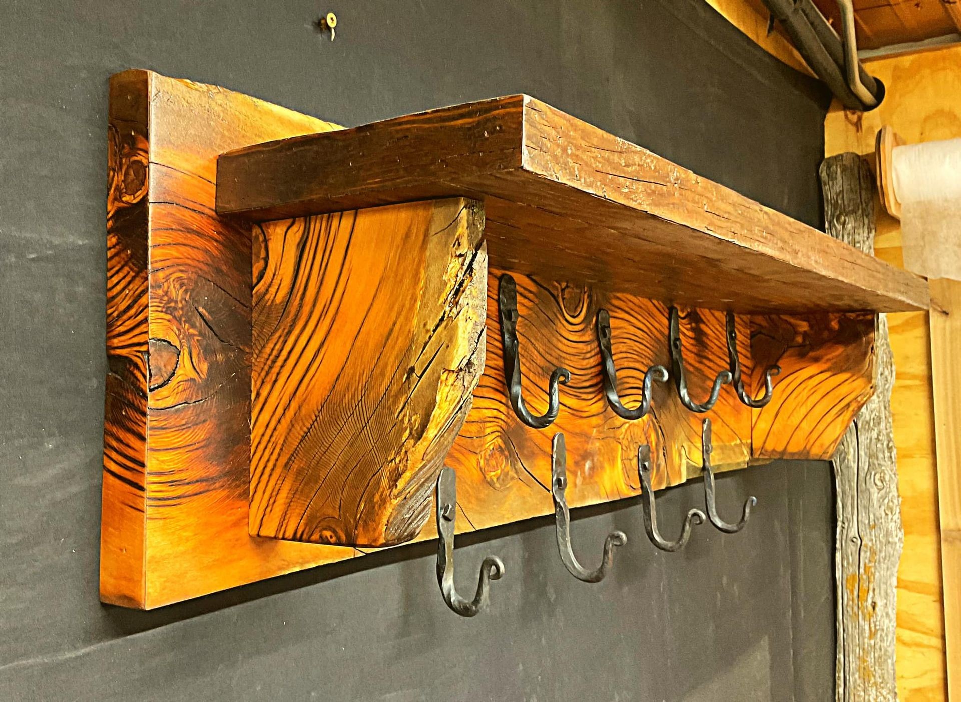 Close-up of a rustic wooden wall shelf with multiple metal hooks for hanging items.