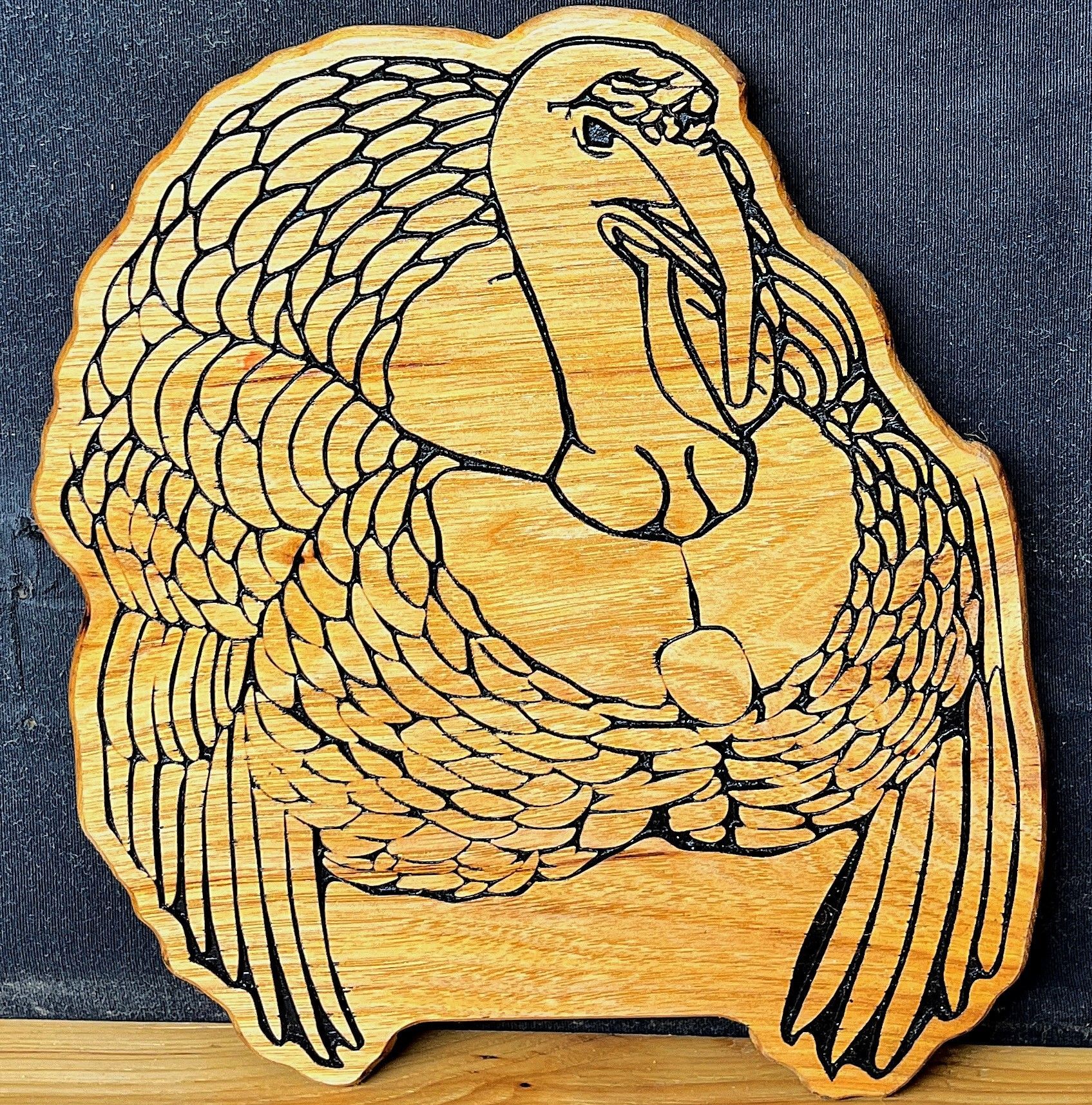 Wooden carving of a bird with intricate detail in its feathers, set against a dark background.