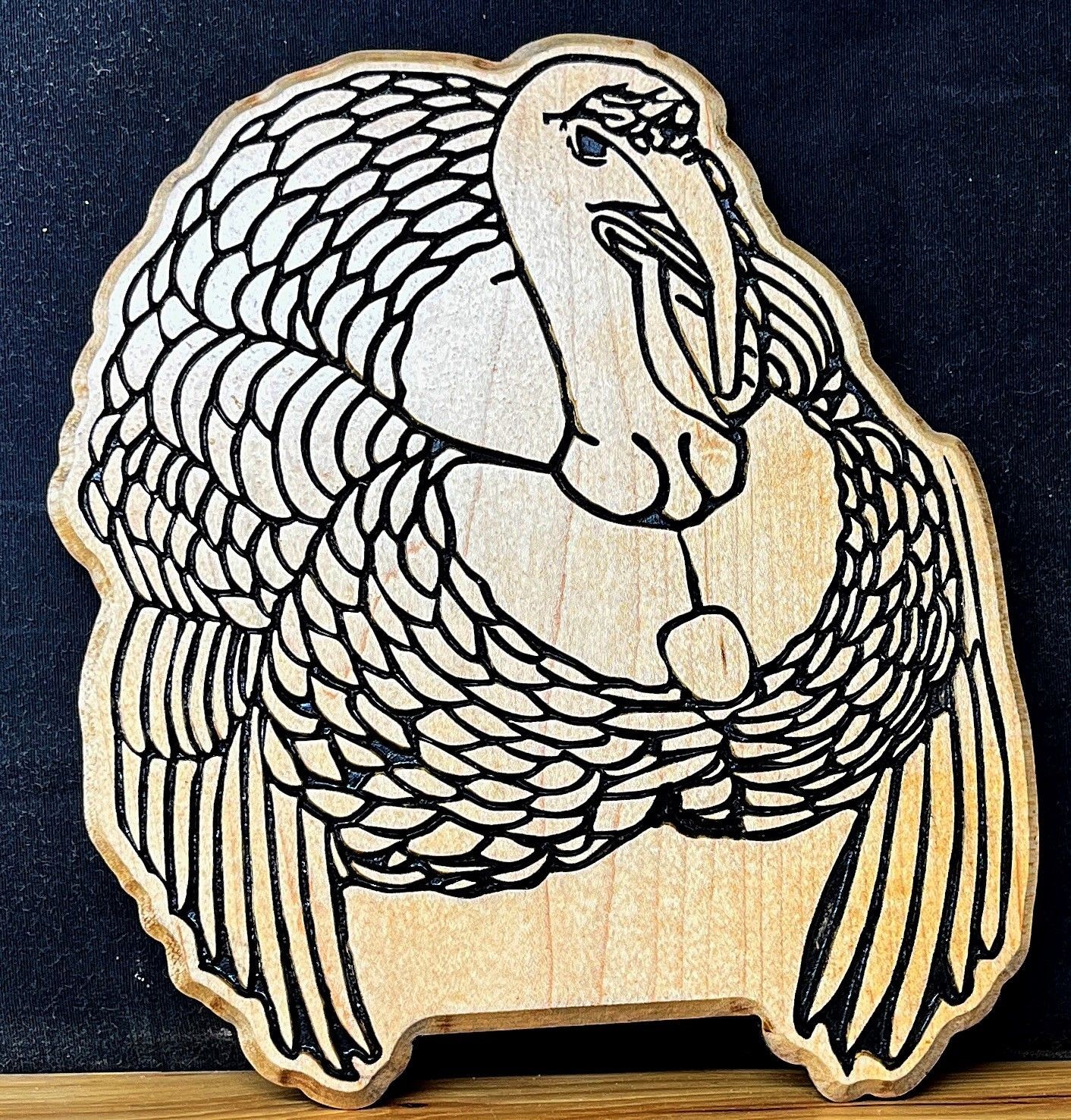 Wooden cutout with a black outline drawing of a stylized bird on a dark background.