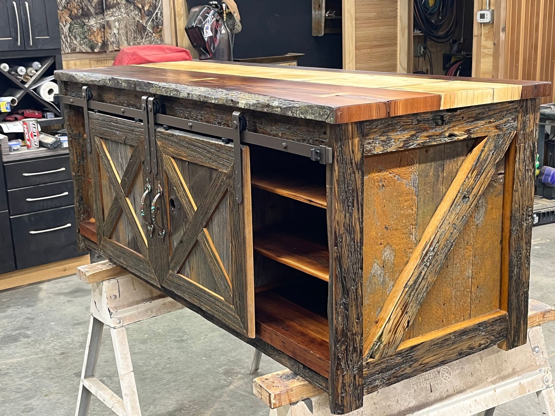 Handcrafted wooden rustic cabinet with sliding barn doors and open shelves in a workshop.