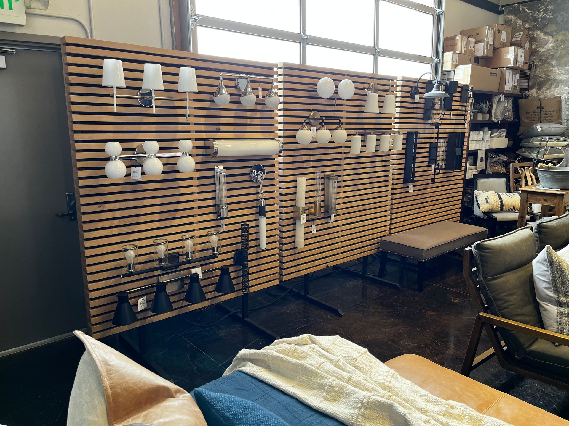 Display of various lighting fixtures mounted on a wooden slat wall in a home decor store.