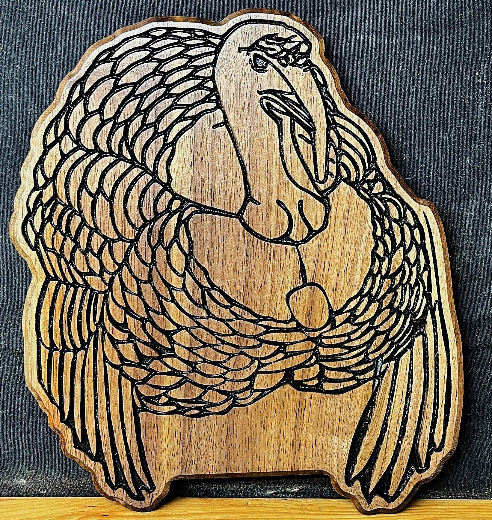 Wooden carving of a bird with intricate feather details on a dark background.