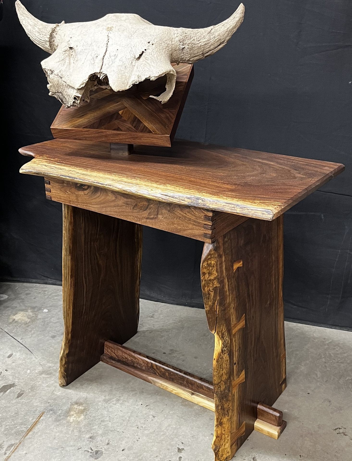 Rustic wooden table with a mounted animal skull featuring long horns, displayed against a dark background.